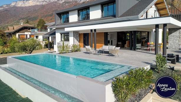 Une maison moderne à deux étages, dotée d’une grande piscine, d’un espace extérieur aménagé et offrant une vue sur les montagnes.