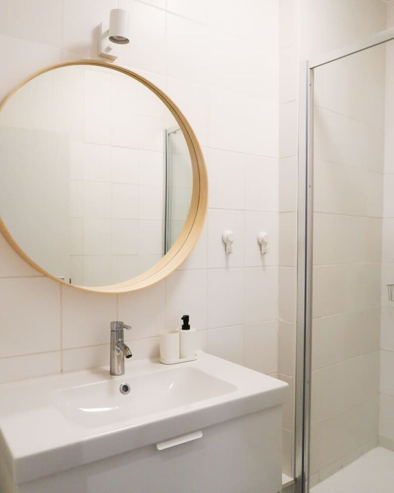 Een badkamer met een witte wastafel, een ronde spiegel en een douchecabine met glazen wanden.