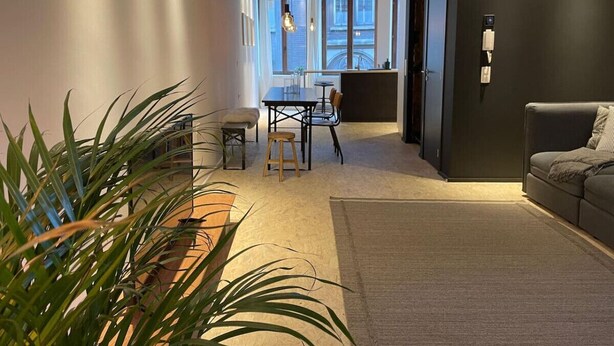 Uma sala de estar moderna com um sofá, uma área de jantar com mesa e cadeiras, e uma janela grande que oferece luz natural.