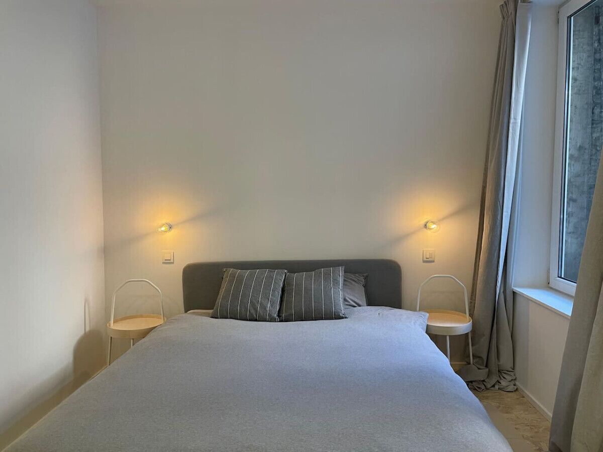 Een slaapkamer met een bed, twee nachtkastjes, een raam met gordijnen en wandlampen.