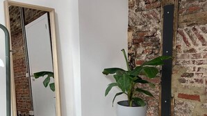 Quarto com um espelho grande, uma planta em vaso sobre um banquinho e uma parede de tijolos.