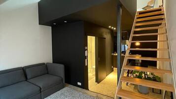 A modern living room with a dark sofa, a patterned rug, and a wooden staircase leading to an upper level.