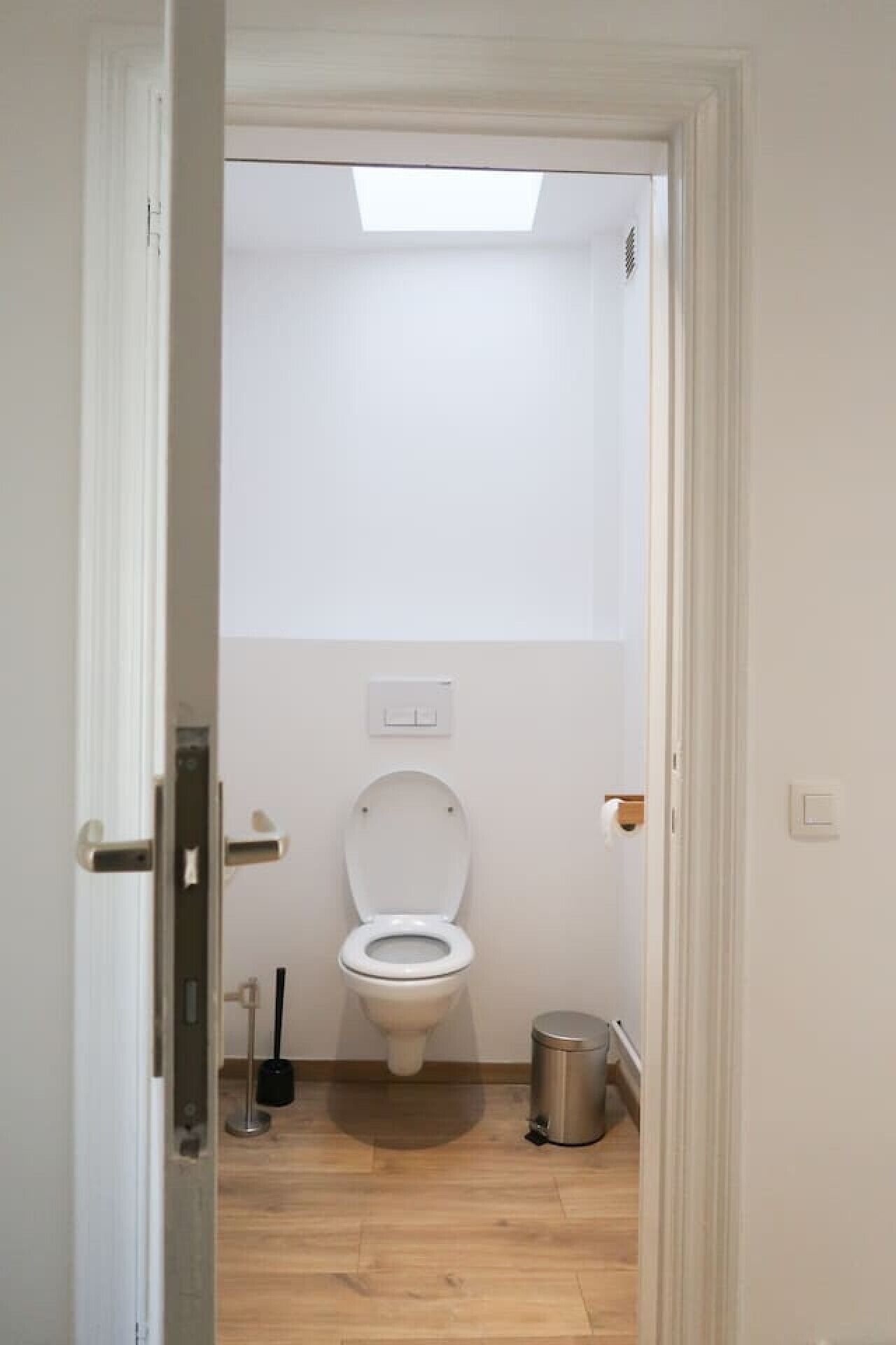 Een kleine, smalle badkamer met een toilet, een prullenbak en een bezem.
