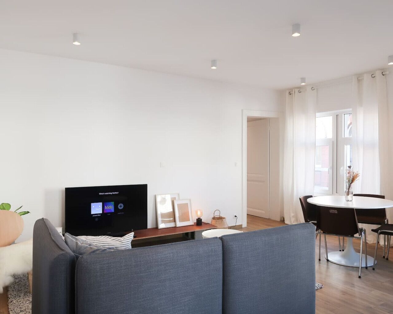 Un salon moderne avec un téléviseur à écran plat, un canapé, une table à manger avec des chaises et une fenêtre avec des rideaux.
