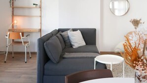 A modern living room with a grey sofa, a round mirror, and a small table with a vase of dried flowers. - Beautiful apartment in Liège center - 2nd floor (Liège)