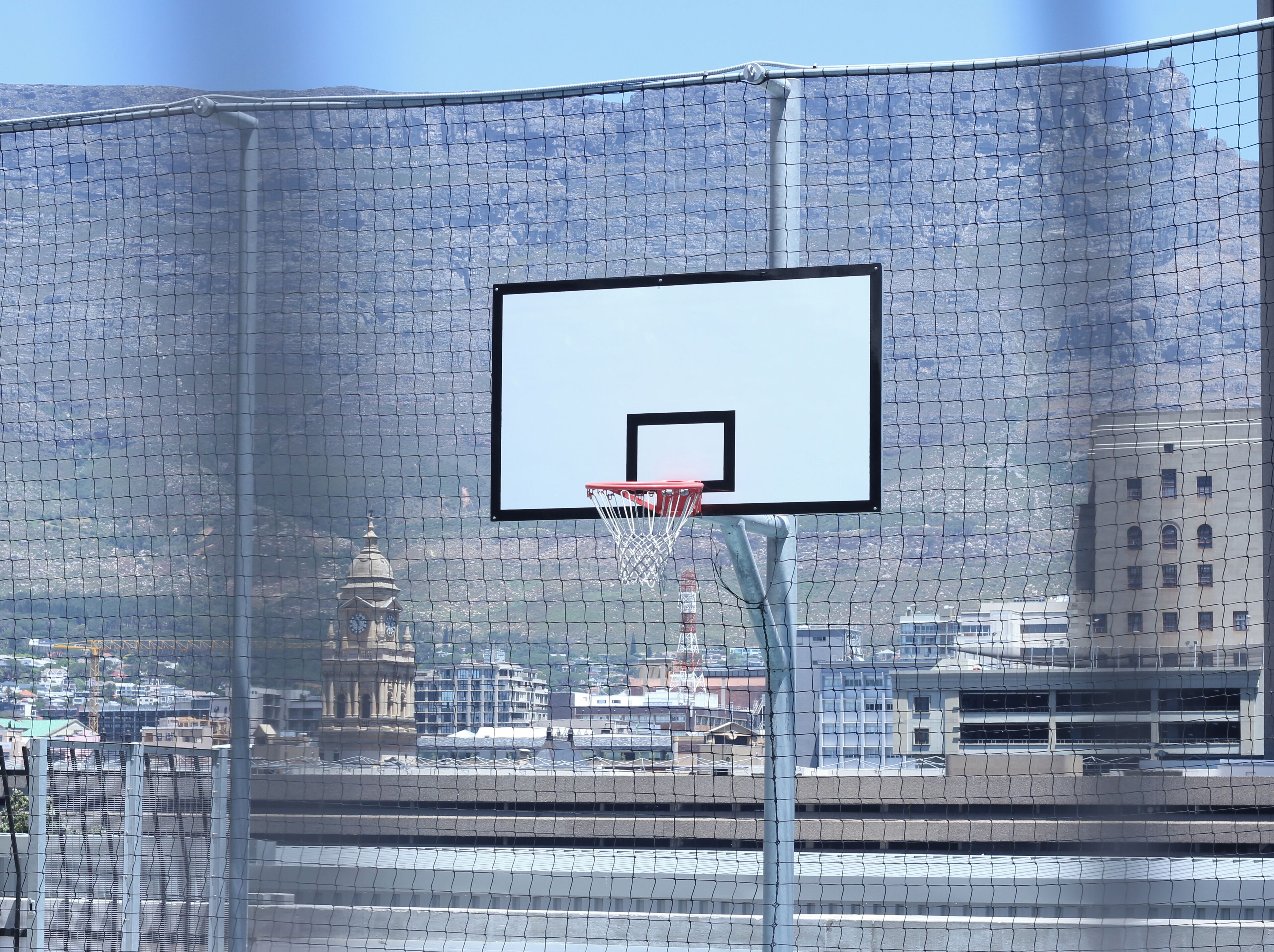 A basketball court with a netted enclosure, a basketball hoop, and a clock tower in the background.