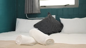 Un lit avec du linge de lit blanc, une serviette blanche roulée et un coussin à motifs noir et blanc.
