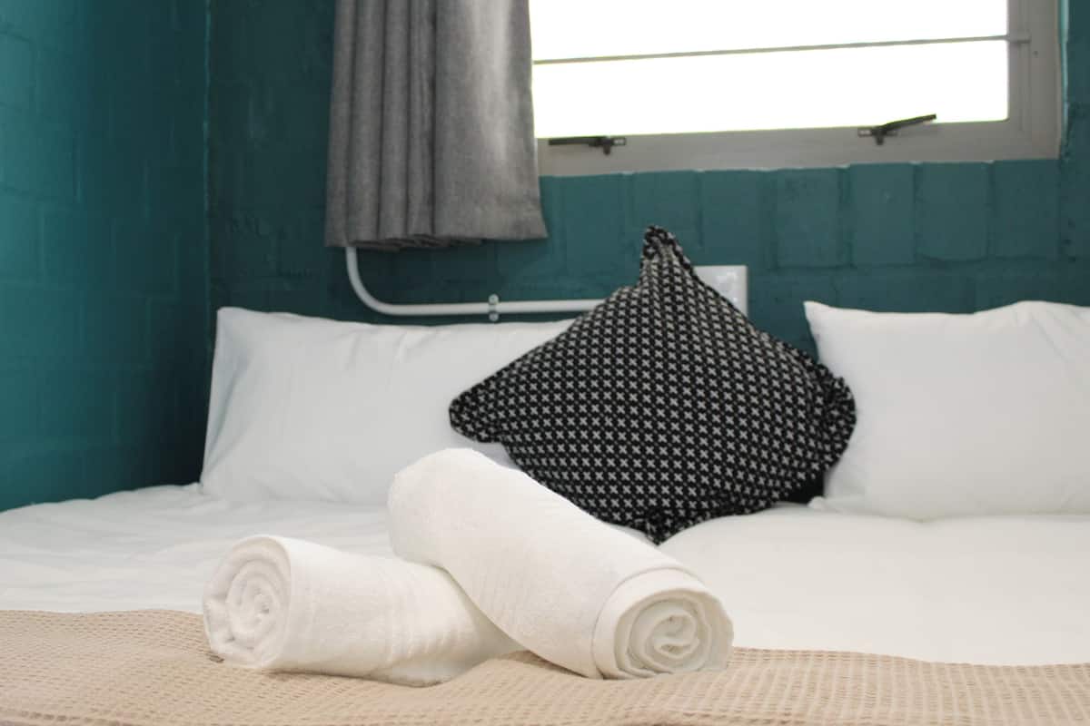 A bed with white linens, a rolled white towel, and a black and white patterned pillow.