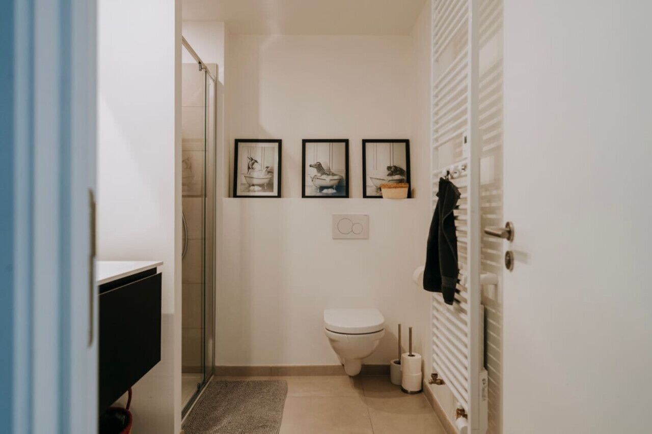 A small bathroom with a toilet, a shower, and a sink. There are three framed pictures on the wall.