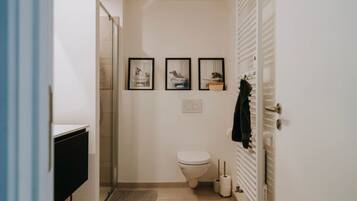 A small bathroom with a toilet, a shower, and a sink. There are three framed pictures on the wall.