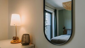 A bedroom with a round mirror, a bedside lamp, and a small table with decorative items. - Apt. 2 chambres + garage en plein centre de Liege (Liège)