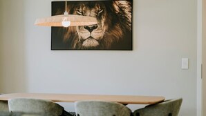 Ein Essbereich mit einem langen Tisch, vier Stühlen, einer Pendelleuchte und einem Bilderrahmen mit einem Löwen an der Wand.