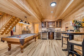 A wooden interior with a pool table, a bar area, and a staircase.