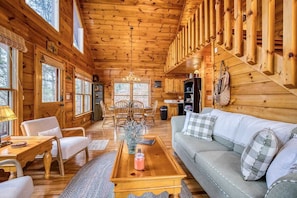 A log cabin interior with a dining area, a sofa, and a chandelier.