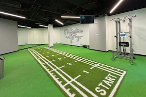 Ein Fitnessraum mit einem grünen Tartanlaufsteg, Gewichtstrainingsgeräten und motivierenden Sprüchen an der Wand.
