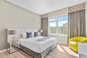 Ein modernes Hotelzimmer mit einem großen Bett, einem Nachttisch mit Lampe, einem leuchtend gelben Sessel und einem Fenster mit Blick auf die Stadt.