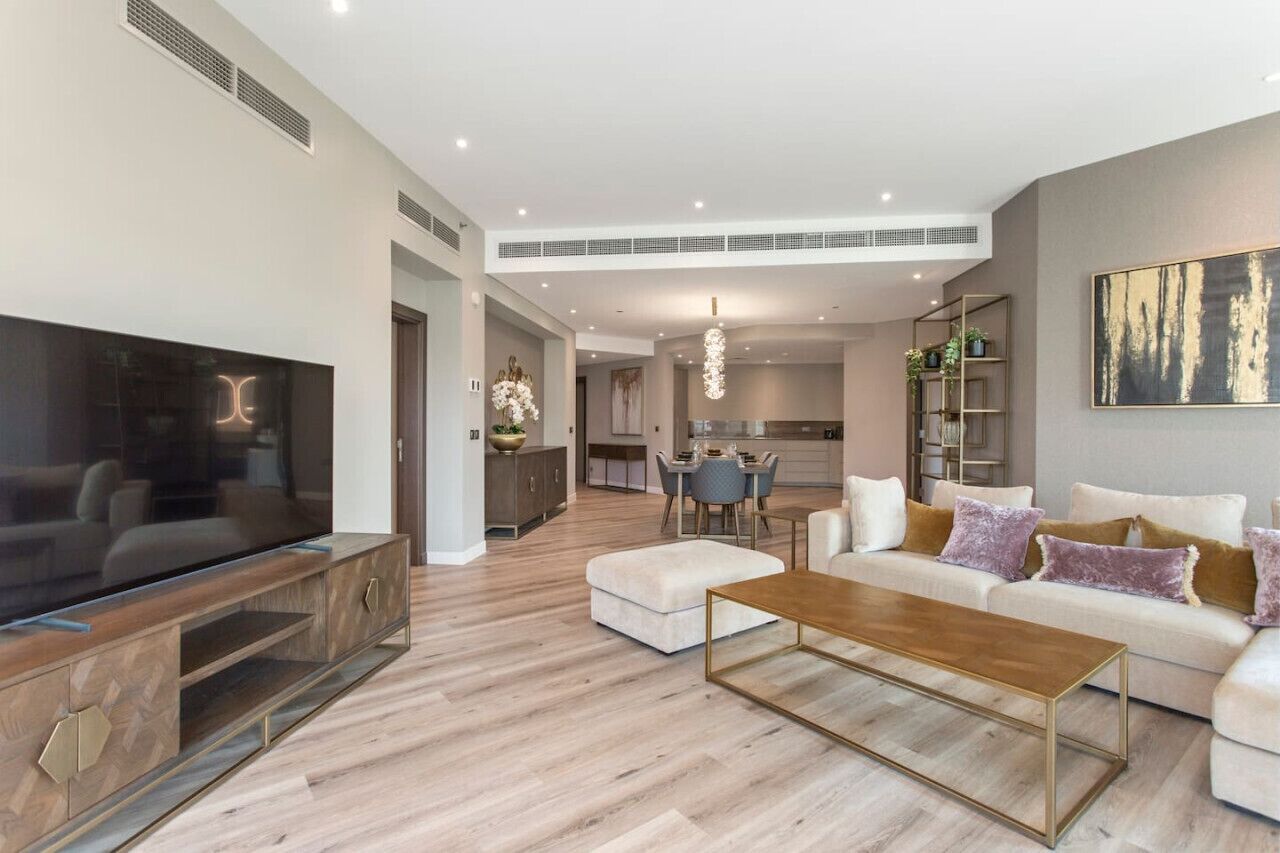 A modern living room with a large flat-screen TV, a wooden entertainment unit, a white sofa with cushions, and a coffee table.