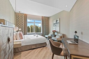 A modern hotel room with a bed, a desk, a chair, and a view of the cityscape through large windows. - Sophisticated 3 Bed Palm Jumeirah w Beach Access (Dubai)