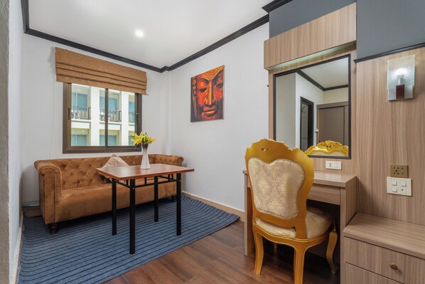 A modern room with a sofa, a dining table, a chair, a desk, a mirror, and a window with blinds. - Lucky City Hotel (Vientiane)
