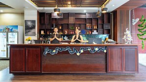 A reception desk with two staff members, wooden paneling, and a decorative garland. - Lucky City Hotel (Vientiane)