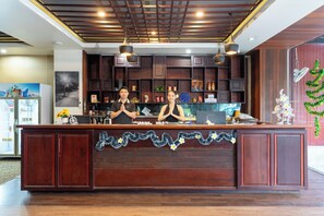 A reception desk with two staff members, wooden paneling, and a decorative garland. - Lucky City Hotel (Vientiane)