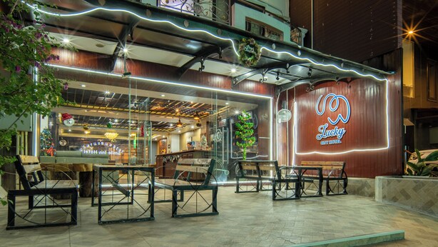 A hotel with outdoor seating, a neon sign, and a glass facade. - Lucky City Hotel (Vientiane)