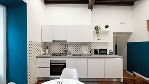 A modern kitchen with white cabinets, a built-in oven, and a microwave. There is a dining table with chairs and a small plant on the countertop. - Domus Maggiore Apartment (Roma)
