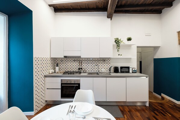 A modern kitchen with white cabinets, a built-in oven, and a microwave. There is a dining table with chairs and a small plant on the countertop.