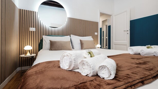 A modern hotel room with a large bed, a round mirror, and a brown throw blanket. - Domus Maggiore Apartment (Roma)