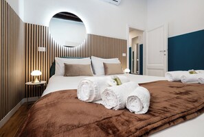 A modern hotel room with a large bed, a round mirror, and a brown throw blanket.