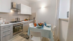 A modern kitchen with stainless steel appliances, a dining table set with plates and glasses, and a light blue tablecloth. - Little Mermaid of Stresa (Stresa)