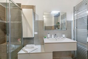A modern bathroom with a glass shower enclosure, a large sink with a mirror, and a towel rack.