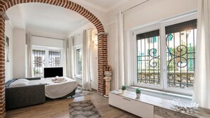 Une chambre moderne équipée d’un lit, d’une télévision, d’une fenêtre avec des barreaux en métal et d’une arche en briques.
