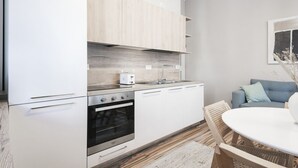 A modern kitchen with white cabinets, a built-in oven, and a toaster. There is a dining area with a round table and chairs.