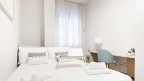A hotel room with a bed, a desk, a chair, a laptop, and a window with curtains.