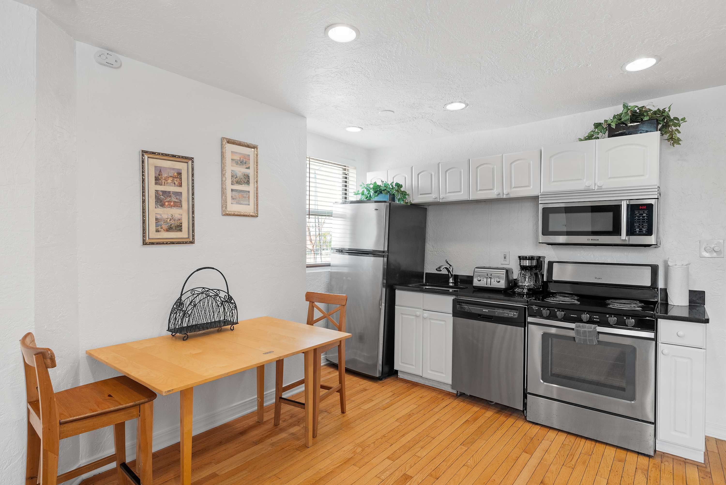 A modern kitchen with white cabinets, stainless steel appliances, a wooden dining table, and two chairs.