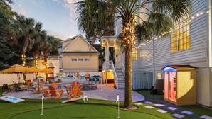 Un patio trasero con césped artificial, una piscina, sillones de descanso y una casita de juegos de madera.