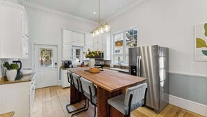 Una cocina moderna con armarios blancos, una isla de madera, taburetes de bar, un refrigerador de acero inoxidable y una lámpara colgante.