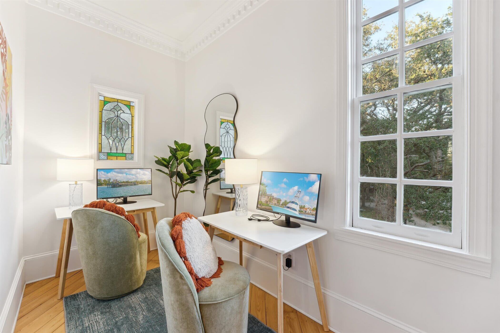 A room with a desk, two chairs, a TV, a lamp, and a window with a view of trees.