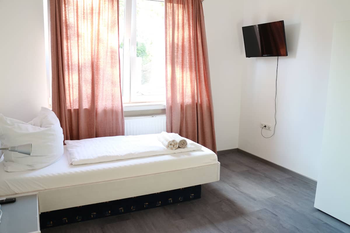A hotel room with a bed, curtains, a TV mounted on the wall, and a window.