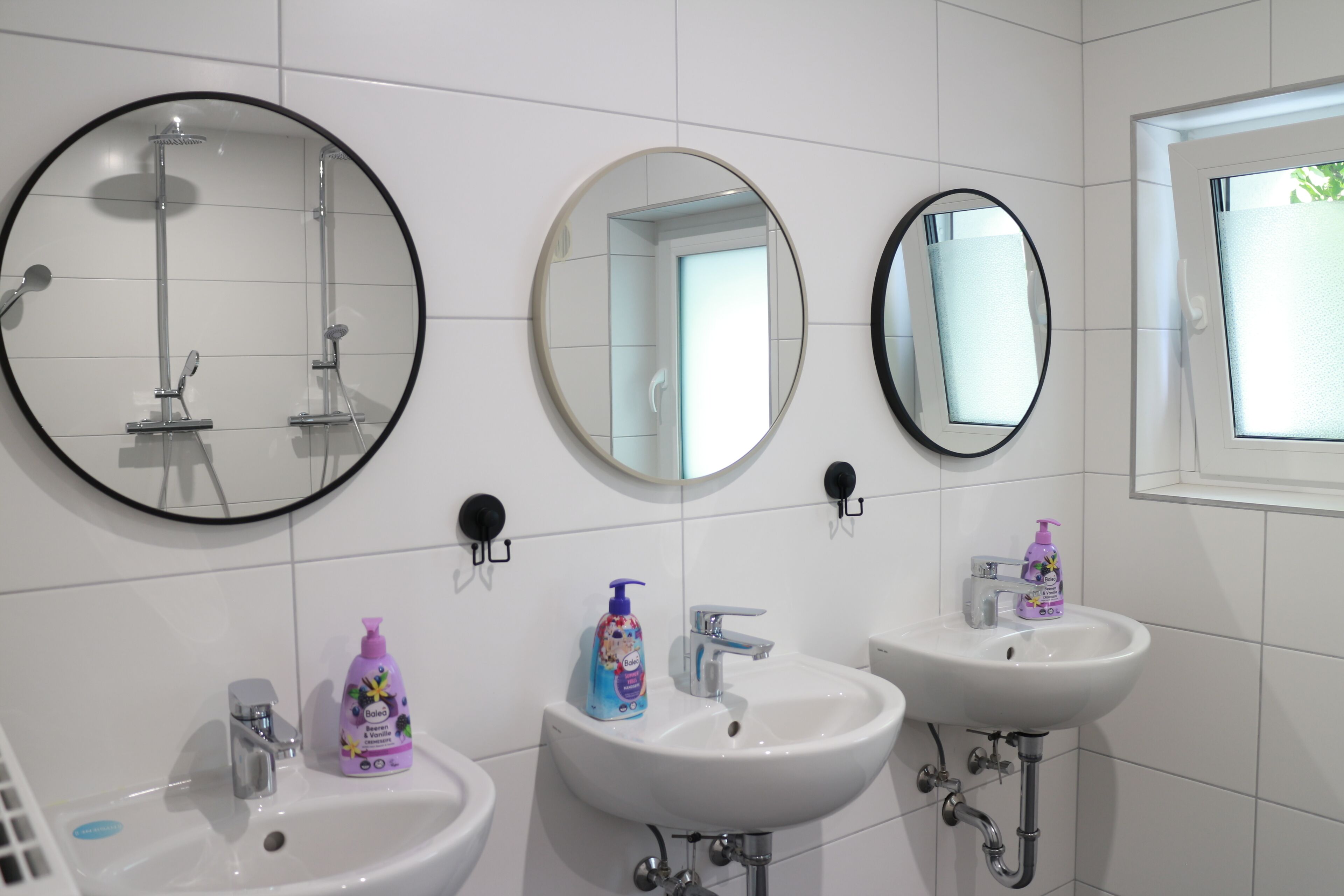 Ein Badezimmer mit drei Waschbecken, zwei runden Spiegeln und einer Dusche.