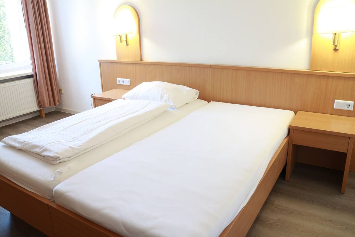A single-bed room with a wooden headboard, two bedside tables, and wall-mounted lamps.