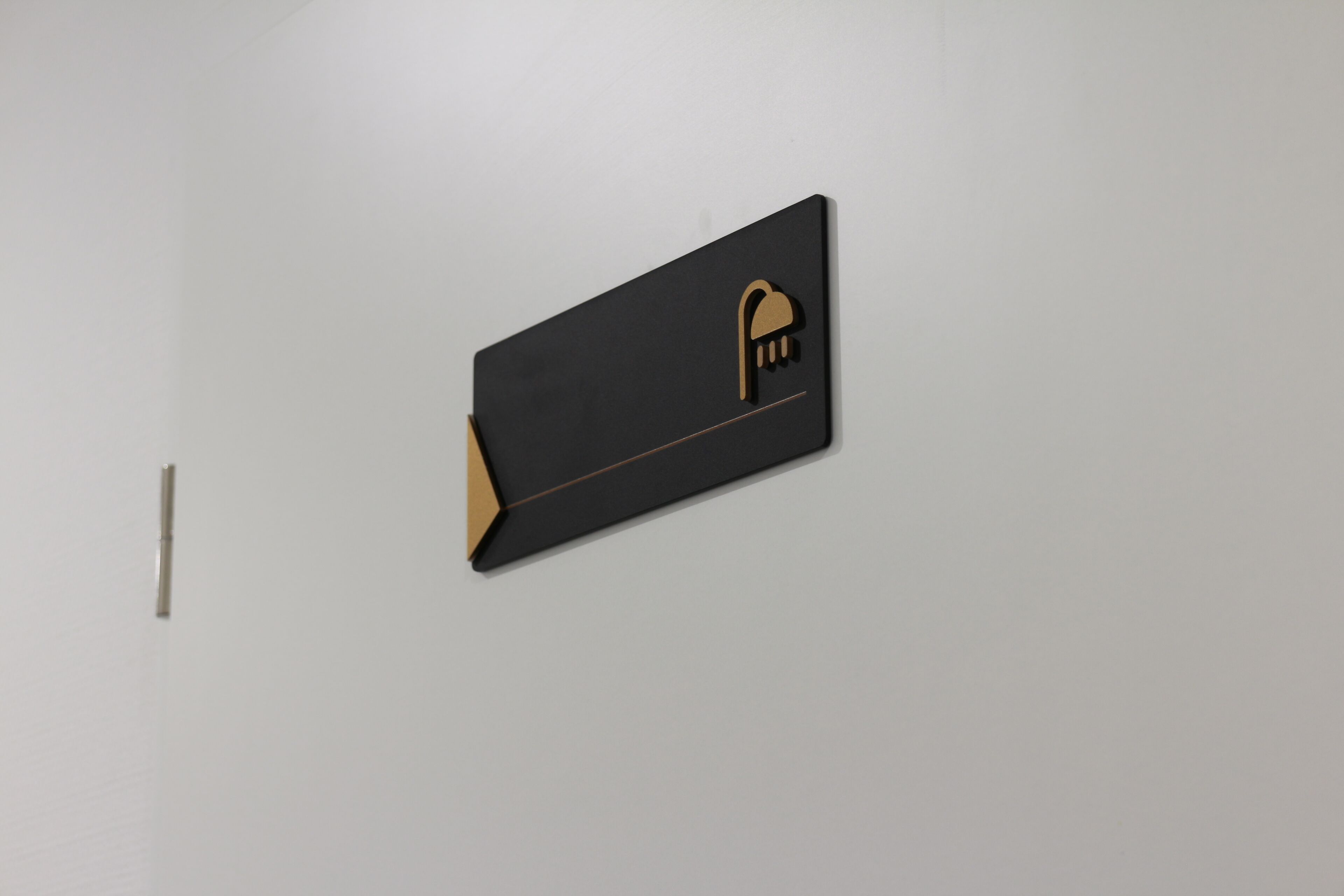 A black, rectangular object with a gold outline and a symbol resembling a hand holding a key, mounted on a white wall.