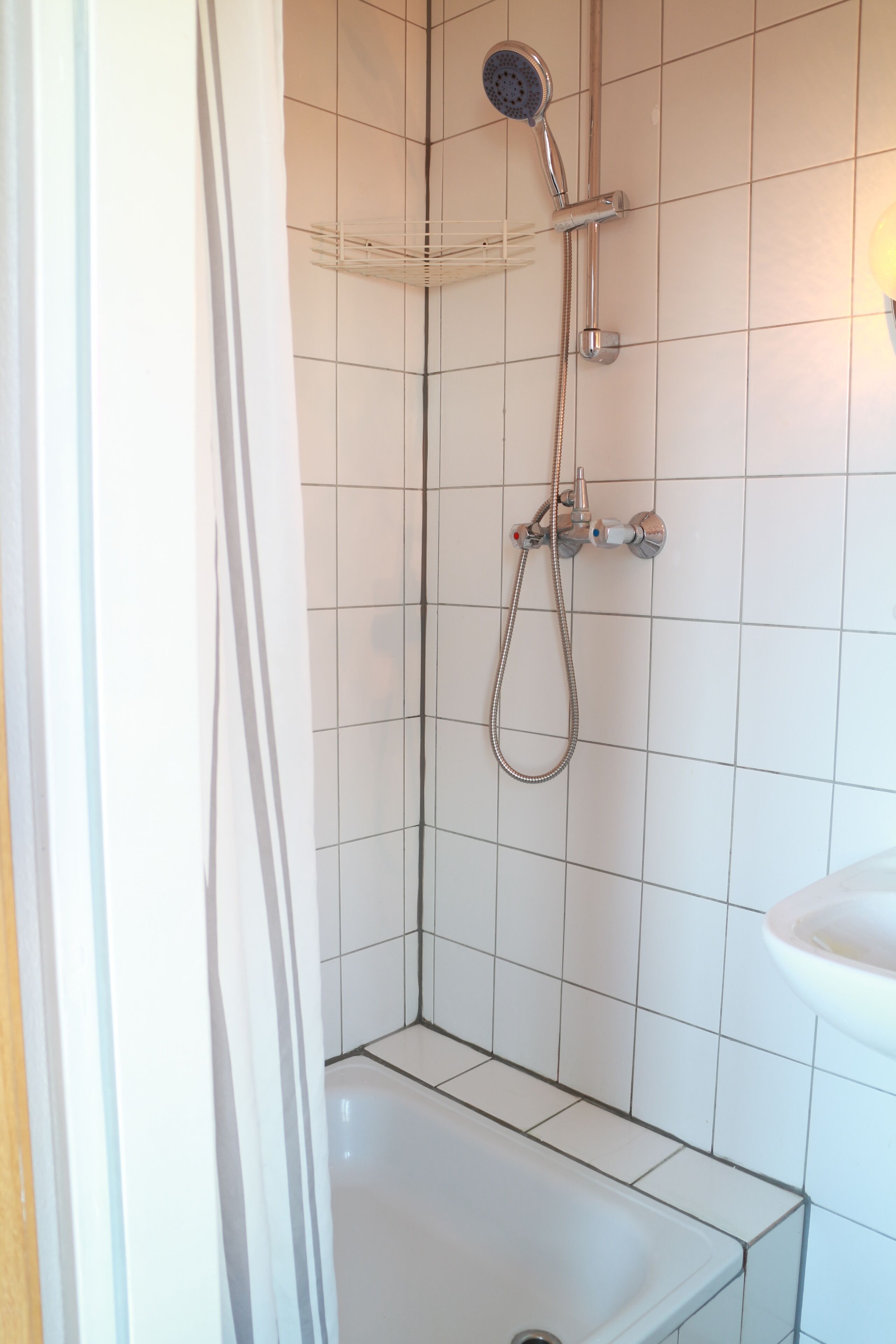 A shower with a handheld showerhead and a wall-mounted faucet.