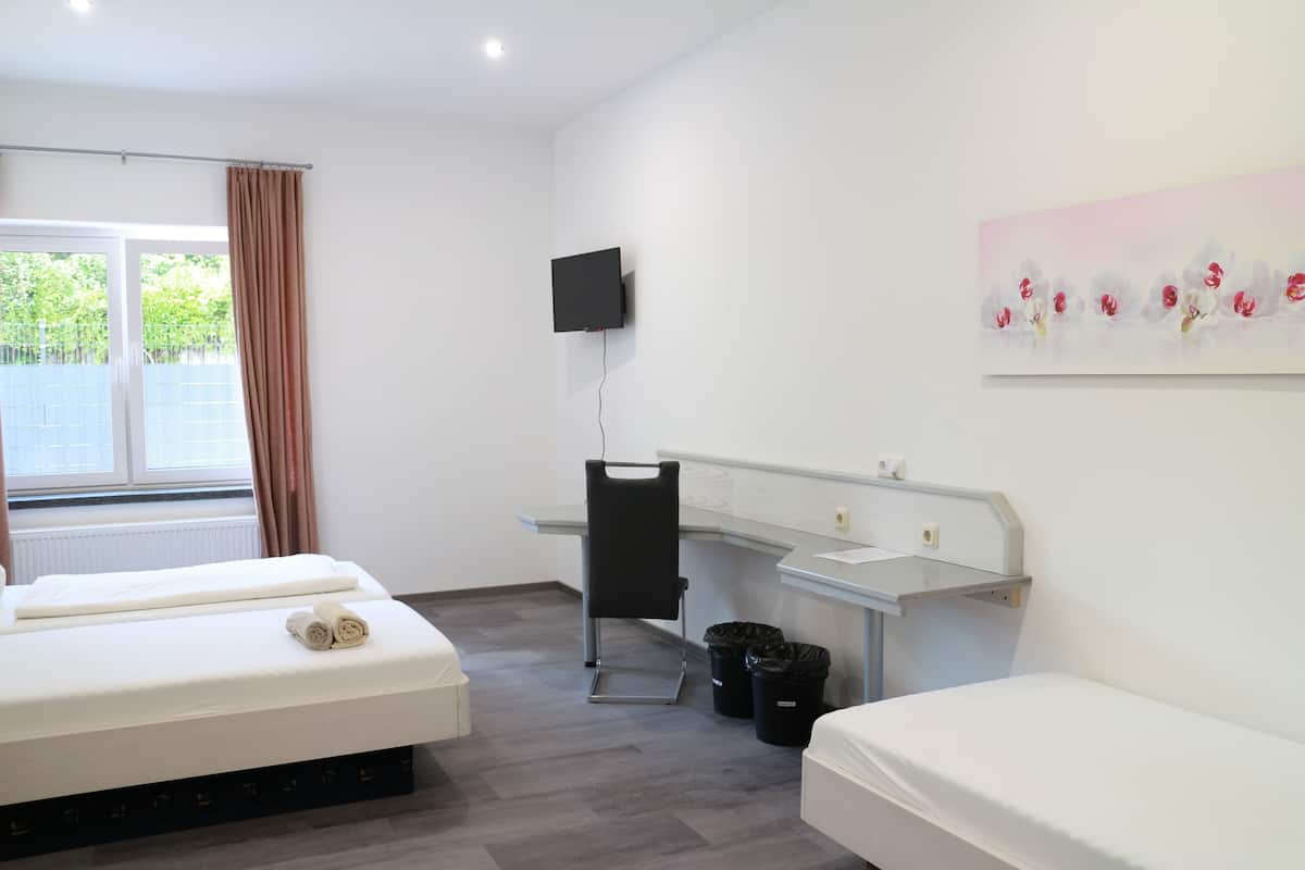A hotel room with a bed, a desk, a chair, a TV mounted on the wall, and a window with curtains.