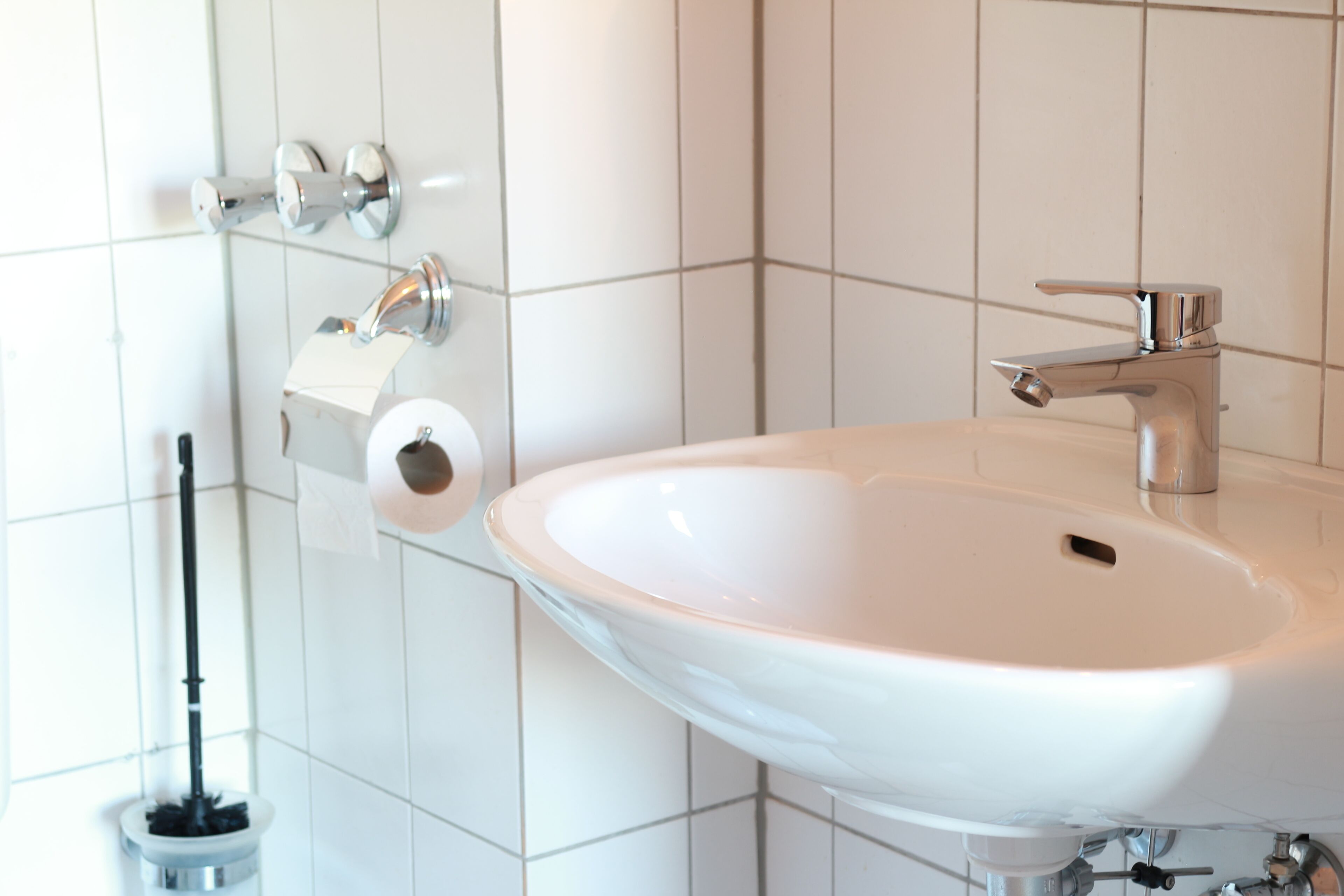 Un baño con un lavamanos blanco, un dispensador de papel higiénico y un cepillo para el inodoro.