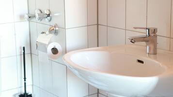 Un baño con un lavamanos blanco, un dispensador de papel higiénico y un cepillo para el inodoro.