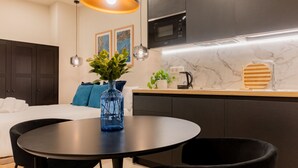 A modern kitchen with dark cabinets, a microwave, and a marble countertop. There is a round dining table with black chairs and a blue vase with green plants. - Estudio Oriente - Design et confort dans DELICIAS MADRID (Madrid)