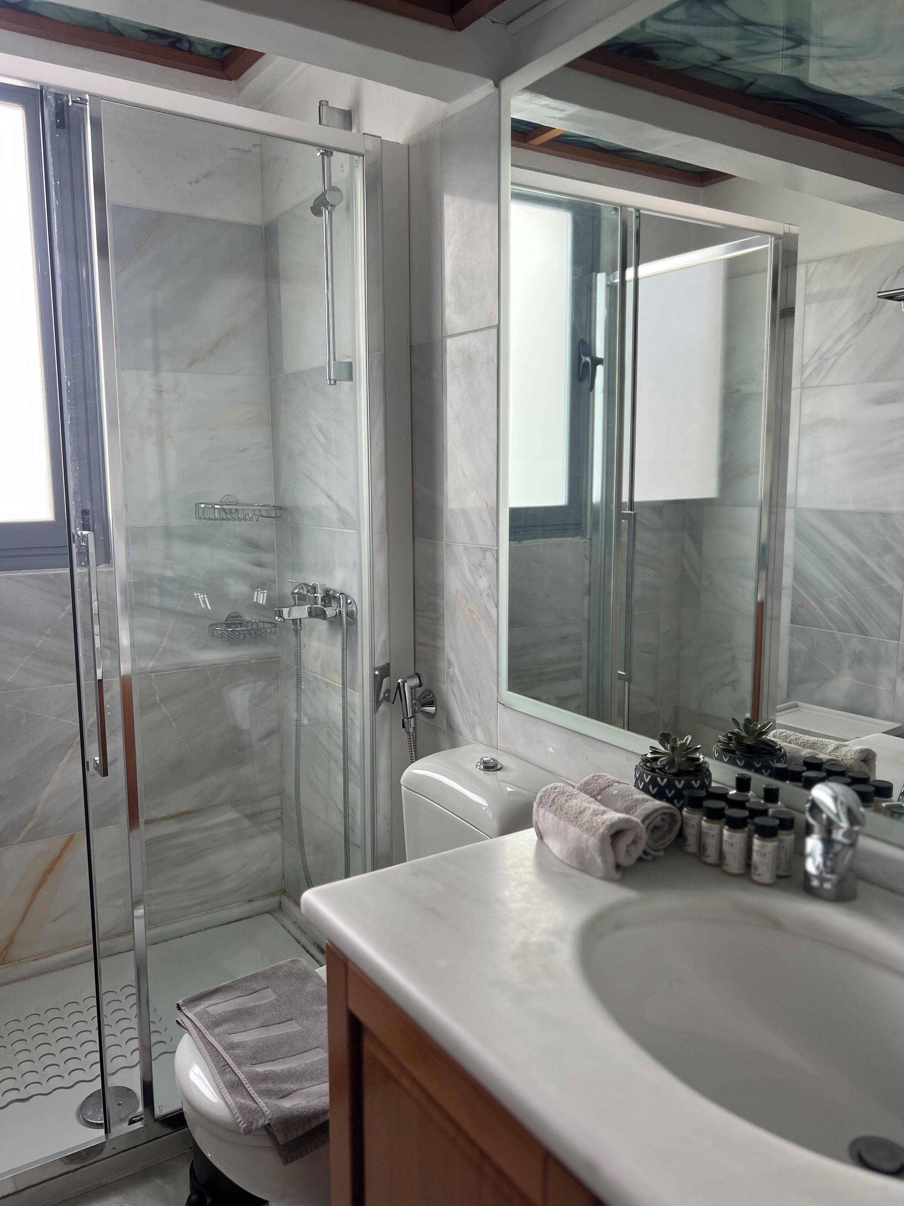 Een moderne badkamer met een douchecabine van glas, een grote spiegel en een marmeren wastafelblad.