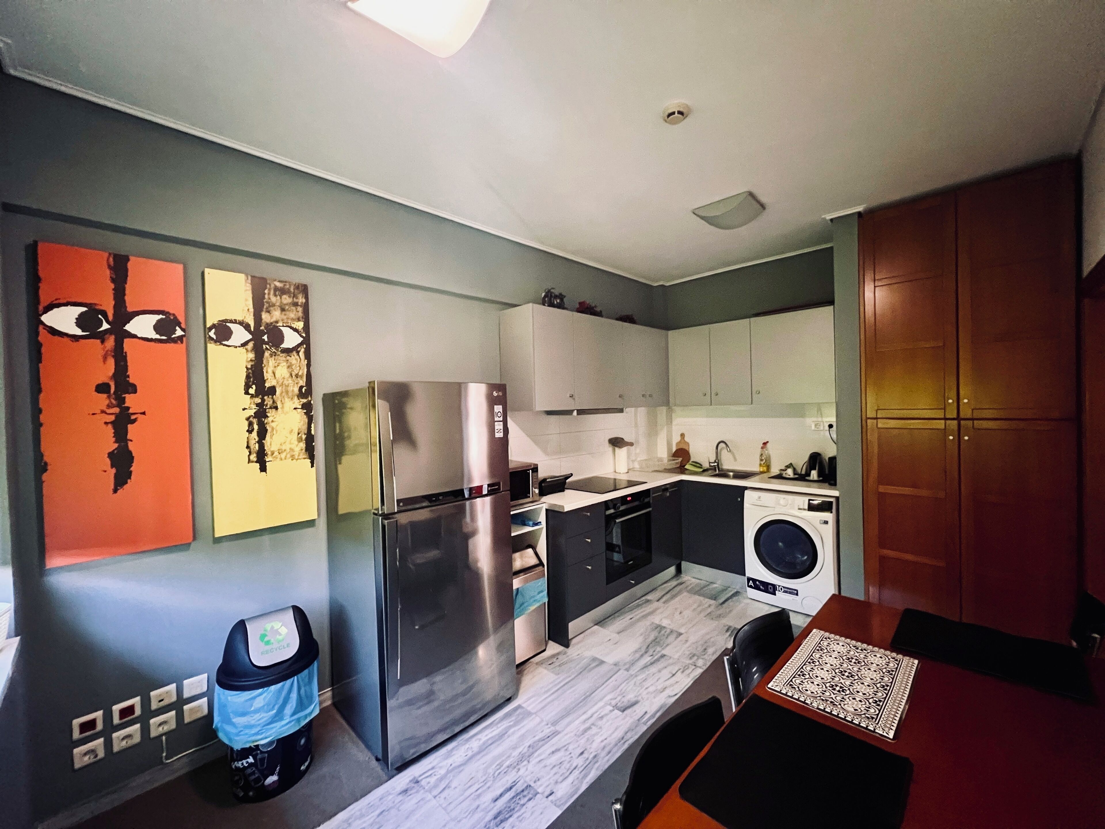 A modern kitchen with a stainless steel refrigerator, a washing machine, and a dining area with a table and chairs.